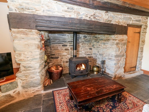 A stone fireplace with a wood-burning stove, a wooden table, and a basket of firewood.