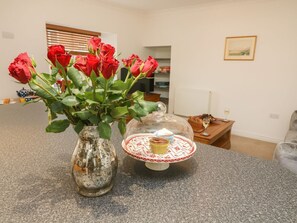 A vase with red roses on a kitchen counter, a glass cake stand with a cupcake, and a dining area in the background. - 2 Eden Lodge, Kirkby Stephen (Kirkby Stephen)