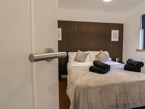 Quarto de hotel com uma cama, cabeceira de madeira, porta com puxador e uma janela.