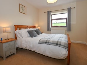 Une chambre à coucher avec un lit en bois, une table de chevet avec une lampe, une fenêtre avec des rideaux et un tableau encadré au mur.