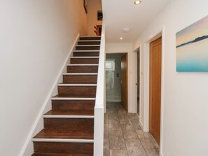 Un escalier menant à un deuxième étage, un couloir avec une porte en bois et un tableau accroché au mur.