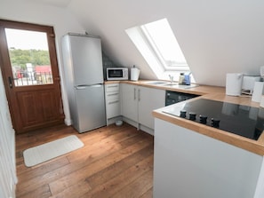 Una cocina funcional con refrigerador, microondas y estufa, piso de madera y tragaluz.