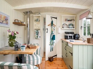 A cozy kitchen with wooden cabinets, a wooden table, a hanging apron, and a coffee machine. - Onnen, near to Aberaeron. 1bed (Llanarth)