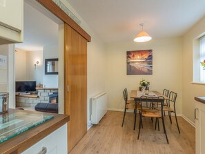 A dining area with a wooden table and chairs, a painting on the wall, and a ceiling light fixture. - Crumstone Corner, Seahouses (Seahouses)