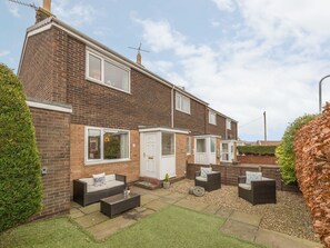 A two-story brick house with a patio area featuring outdoor furniture and a small garden. - Crumstone Corner, Seahouses (Seahouses)