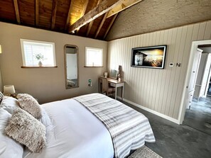A bedroom with a large bed, a desk, a mirror, and a framed picture on the wall.