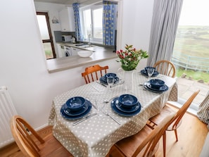 A dining table set for four with blue plates and cutlery, a vase with flowers, and a view of the countryside. - Valley High Retreat in Solva (Haverfordwest)