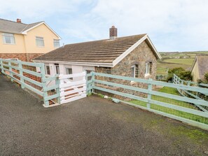 A stone building with a white door, a light blue fence, and a paved driveway. - Valley High Retreat in Solva (Haverfordwest)