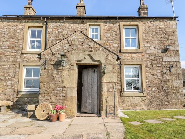 A stone building with a central entrance, windows, and a small garden area with potted plants.