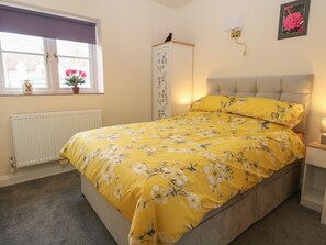 Ein Schlafzimmer mit einem Bett, einem Heizkörper, einem Fenster mit Vorhang, einer Wandlampe und einem Bilderrahmen.