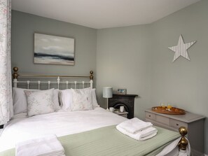Una cama bien tendida con una colcha verde, una mesita de noche con una lámpara, un cuadro enmarcado en la pared y una decoración con forma de estrella.