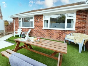 Eine Terrasse mit Holztisch und -stühlen, ein Ziegelhaus und eine kleine Rasenfläche.