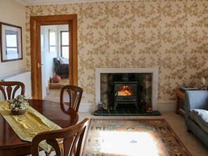 A living room with a fireplace, a dining table with chairs, and a patterned rug. - Seascape, Portknockie (Buckie)