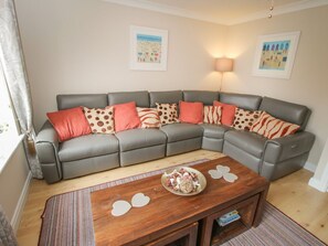 A grey sectional sofa with patterned cushions, a wooden coffee table with a plate of food, and two wall-mounted lamps. - The Shipwrights, Whitby (Whitby)