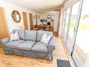 A living room with a grey sofa, wooden flooring, a dining table with chairs, a kitchen in the background, and a large sliding glass door leading to an outdoor area. - Chianti, Seaview Retreat in Pondwell (Ryde)