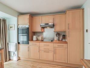 A kitchen with wooden cabinets, a stove, oven, and a microwave. - 7 Press Castle, Coldingham (Eyemouth)