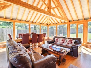 A covered patio area with a wooden ceiling, leather sofas, a dining table with chairs, and a view of a backyard. - Talar Wen, Bala, Gwynedd 3 bed (Y Bala)