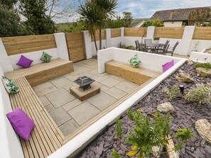 A patio with wooden benches, a table, and a small garden area. - Estuary View, Newquay (Newquay)