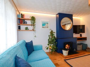 A living room with a blue sofa, a fireplace, a television, and a bookshelf. - Estuary View, Newquay (Newquay)