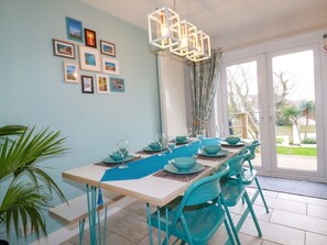 A dining area with a table set for four, teal chairs, and a ceiling light fixture. - Estuary View, Newquay (Newquay)