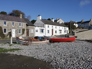 A row of stone buildings with a pebbled beach in front. - Old Tollgate, Llangefni (Holyhead)