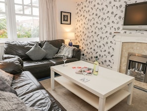 A living room with a leather sofa, a white coffee table, a fireplace, and a TV mounted on the wall.