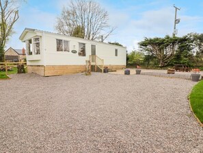 A single-story mobile home with a front porch, a small deck, and a gravel driveway.