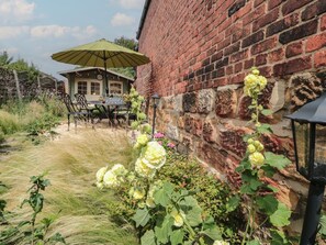 A brick building with a table and chairs under a green umbrella, surrounded by flowering plants. - 98 Westgate is in Guisborough. (Guisborough)