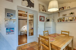 A room with a wooden dining table, chairs, a white refrigerator, and a door leading to another room. - Apartment 'Histoire' with Private Garden and Wi-Fi (Saintes-Maries-de-la-Mer)