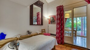 Ein Schlafzimmer mit Bett, Spiegel, Lampe, Fenster mit Vorhängen und Blick ins Freie.