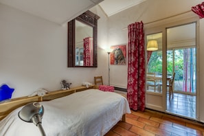 Une chambre Ă coucher avec un lit, un miroir, une lampe, une fenĂȘtre avec des rideaux et une vue sur lâextĂ©rieur.