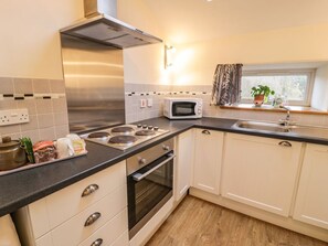 A kitchen with a stove, microwave, oven, and a window with curtains. - Charming Y Bwthyn Retreat in Llanberis (Caernarfon)