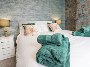 A neatly made bed with green towels, a white nightstand with a lamp, and patterned pillows. - 3 Auborough Street, Scarborough (Scarborough)