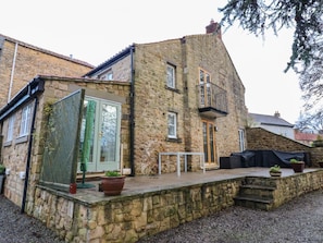 Un bâtiment en pierre doté d’un balcon, d’une porte et d’un petit espace extérieur aménagé pour s’asseoir.