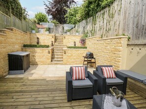 A patio with wicker furniture, a stone wall, and a wooden deck.