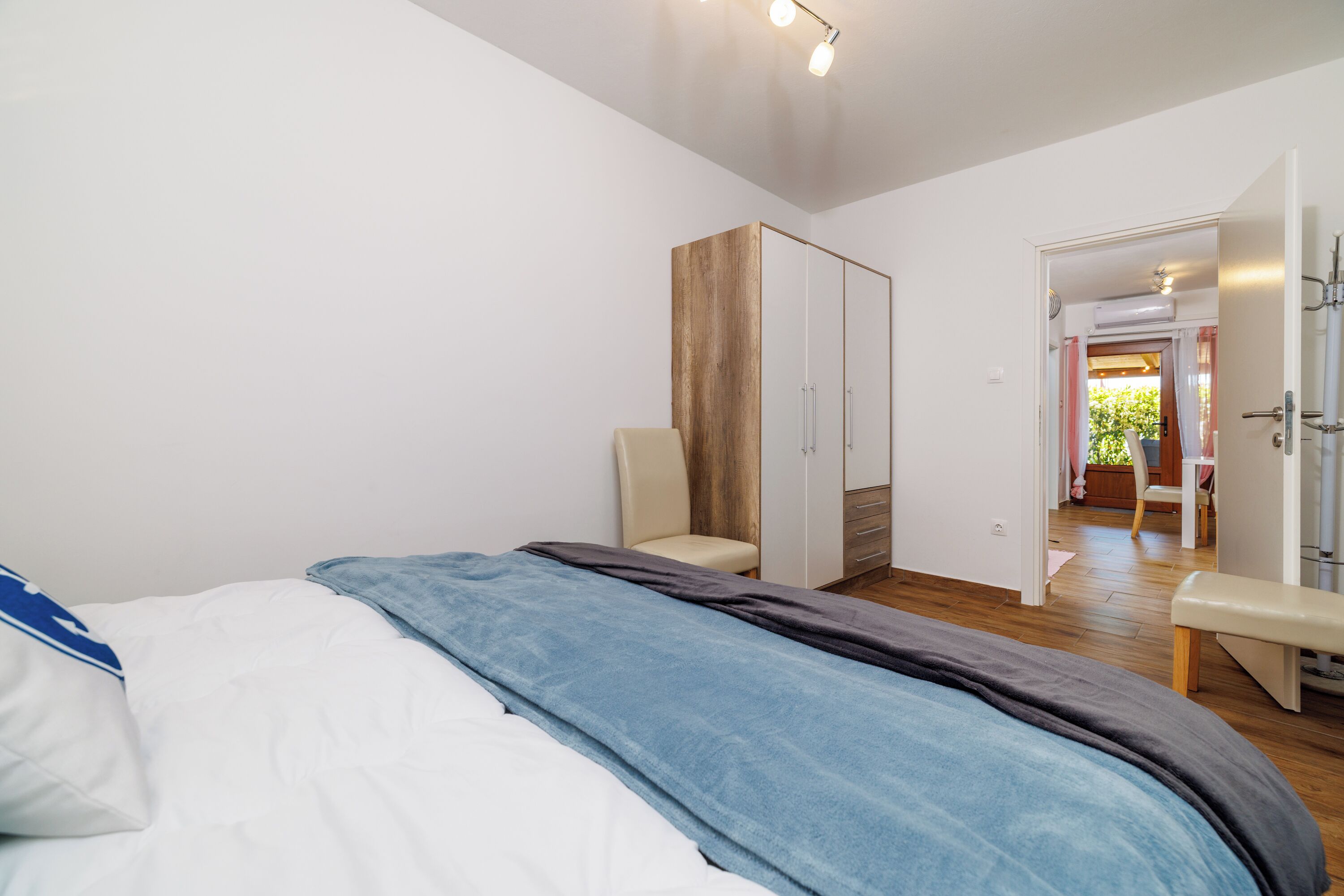 Ein Schlafzimmer mit einem Bett, einem Kleiderschrank, einer Bank und einer Tür zu einem anderen Raum.