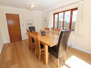Comedor con mesa y sillas de madera, una araña y una ventana con cortinas.