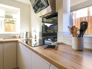 A modern kitchen with a wooden countertop, a built-in stove, and a window with a view of a wooden fence. - Farmer's Rest, Cambridgeshire. (Ely)