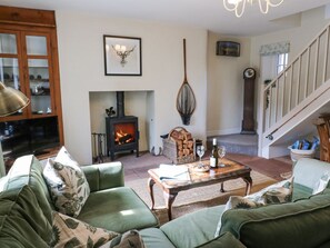A cozy living room with a fireplace, green sofas, a coffee table, and a staircase. - 3 Eden View, Lazonby (Penrith)