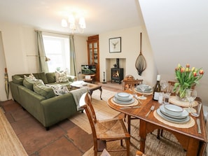 A cozy living room with a sofa, dining table set for four, a fireplace, and a television. - 3 Eden View, Lazonby (Penrith)