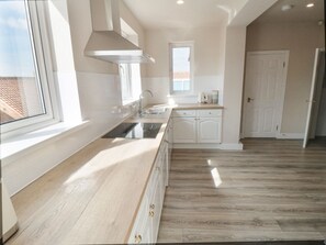 A modern kitchen with a large window, wooden flooring, and white cabinetry. - 11 Castle Gardens, Scarborough (Scarborough)