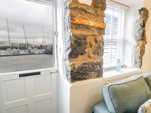 Una habitación con pared de piedra, una ventana con persianas, una puerta blanca y vista a un puerto deportivo.