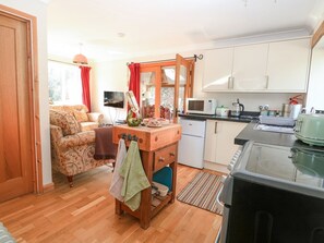 A compact living space with a kitchenette, a sofa, a wooden sideboard, and a television. - The Lodge, Coltishall (Norwich)