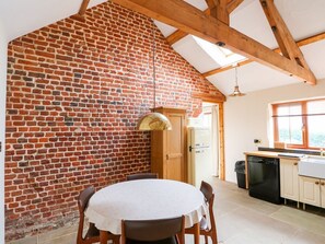 Eine Küche mit Backsteinwand, Holzbalken, einem runden Tisch mit Stühlen und einem Geschirrspüler.