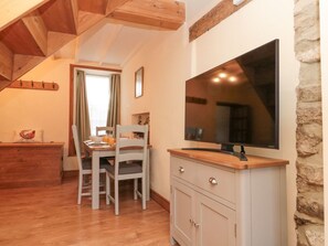 A dining area with a wooden table and chairs, a TV mounted on a stone wall, and a wooden ceiling. - Bay Tree Cottage, Pickering (Pickering)