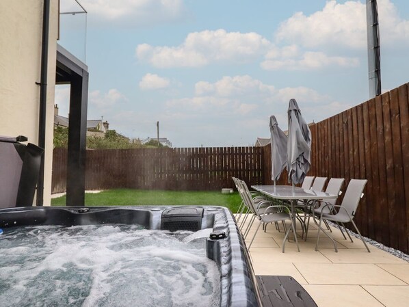 A hot tub with a wooden fence and outdoor furniture in a backyard.