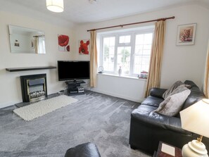 A living room with a fireplace, a television, a sofa, and a window with curtains. - Halcyon Annexe, Benllech (Moelfre)