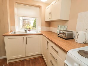 A kitchen with a sink, wooden countertop, white cabinets, a toaster, and a kettle.