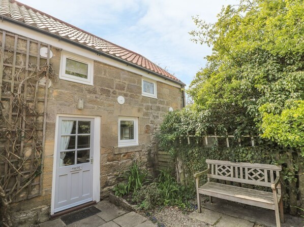 A stone house with a white door, a small window, and a wooden bench in the garden.