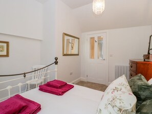 A bedroom with a bed, a chair, a dresser, a door, and a chandelier. - The Old Thatch, Porlock. 1bed. (Minehead)